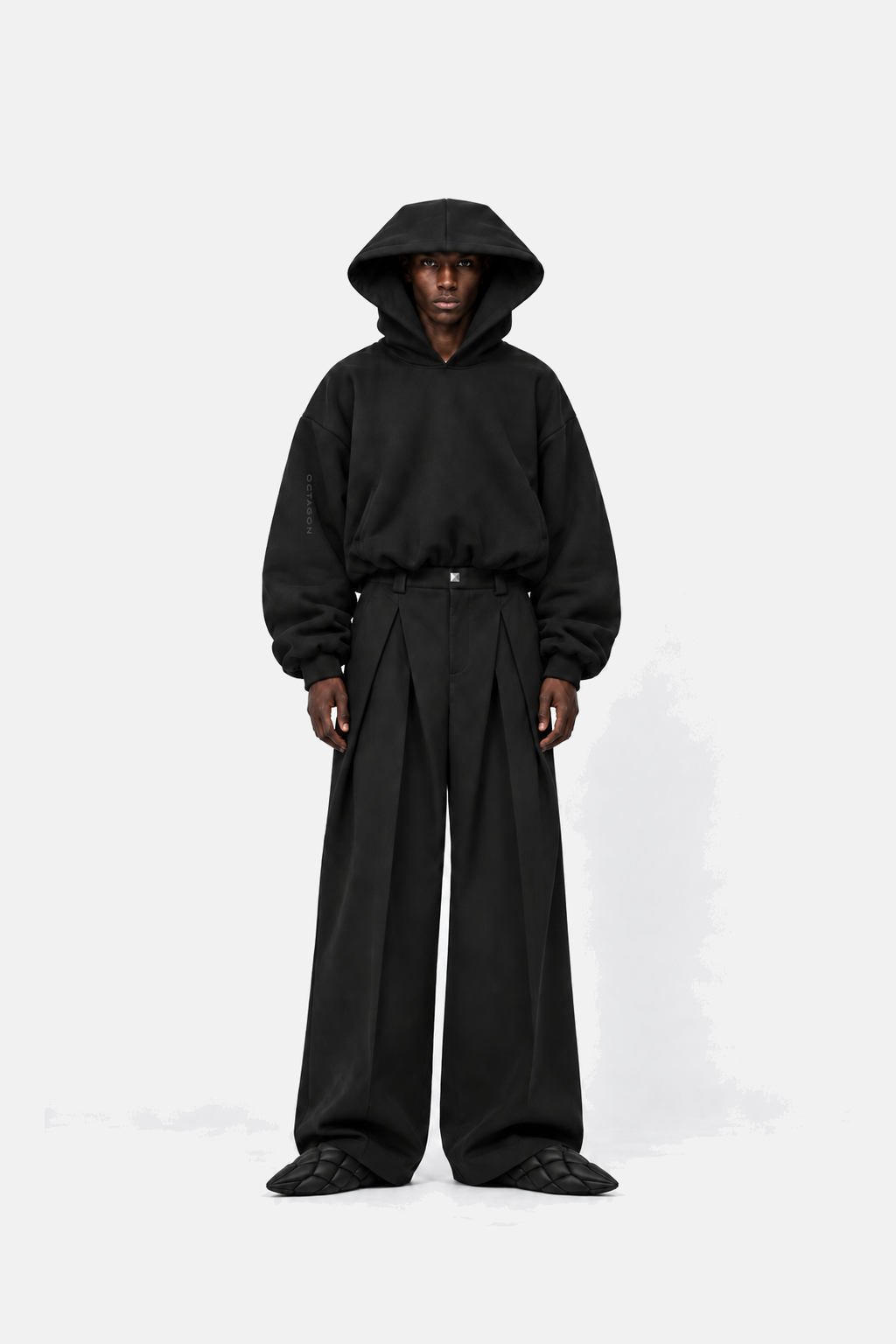 Black runway model wearing Square Hood Hoodie with wide pleated trousers and pointed Octagon shoes, front view