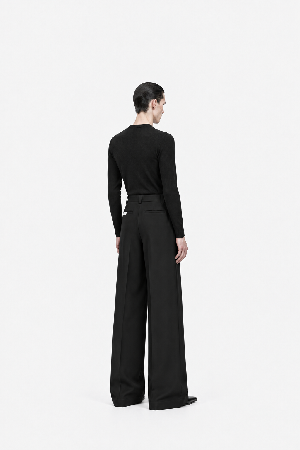 Male model wearing black Octagon double-layer pleated trousers, rear three-quarter view