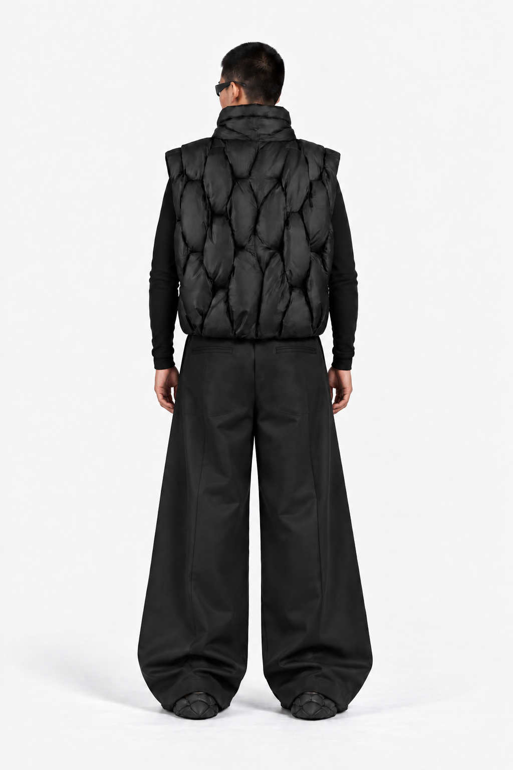 Back view of model wearing the zipper-free OCTAGON Pentagon black puffer vest and graphite Foam Runners